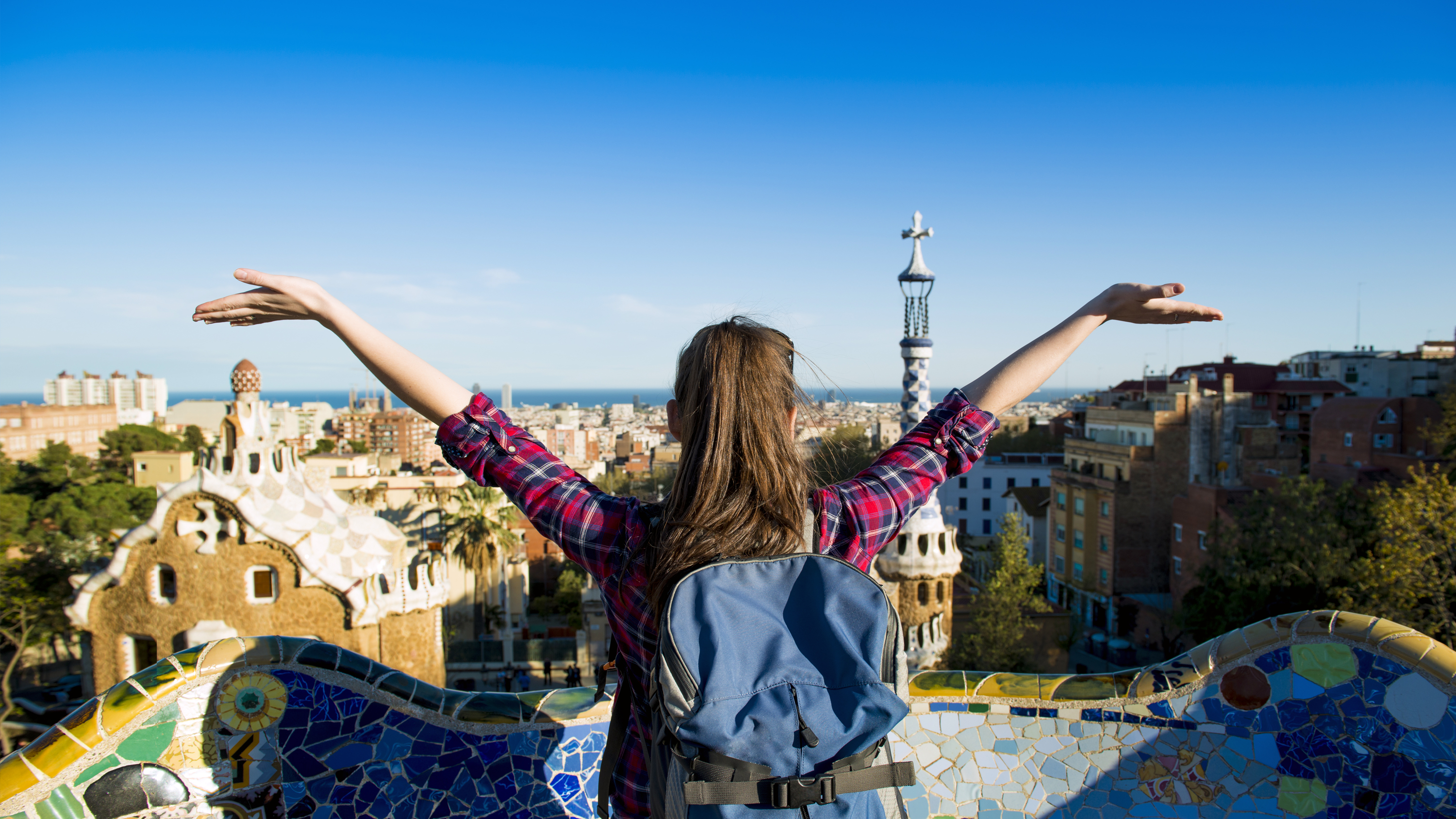 a happy student rejoicing with her arms out, palms facing towards the sky, as she looks over a beautiful city landscape
