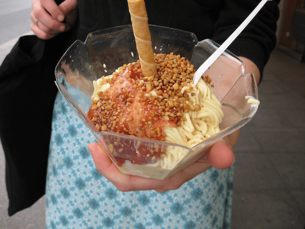 woman holding glass bowl of spagehhti like ice cream, red topping, nuts and wafer stick 