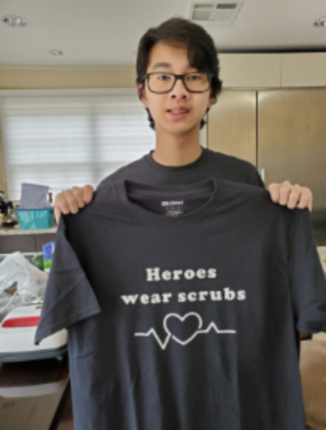 Teenage boy holding up a heroes wear scrubs tshirt