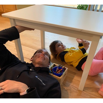 Woman and daughter laying on floor drawing on underside of wooden table 