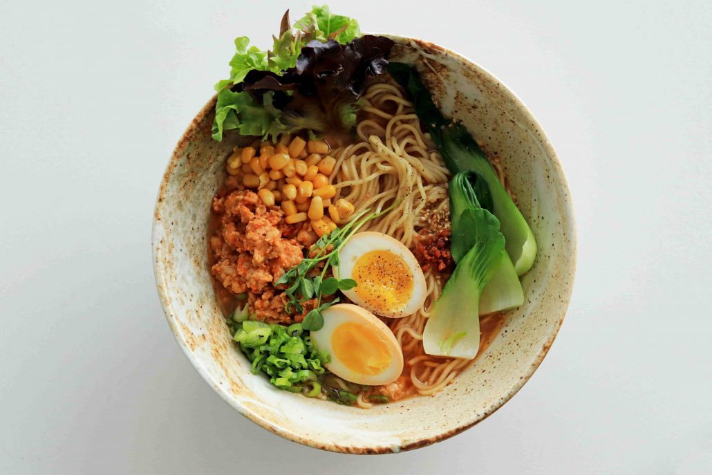 Bowl of ramen containing bok choy, ground meat, corn and marinated egg