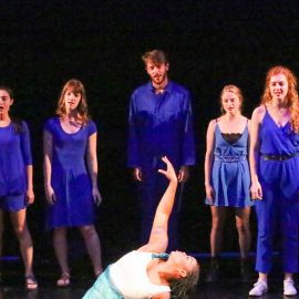 Dancers dressed in bright blue surround a girl dressed with light green and white